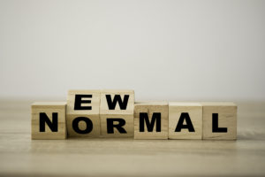 Managing IT concept photo showing wooden blocks with black capital letters sit on a wooden surface, spelling NORMAL with the O and R turned slightly to show E and W on their top sides, overall spelling out the phrase NEW NORMAL. 
