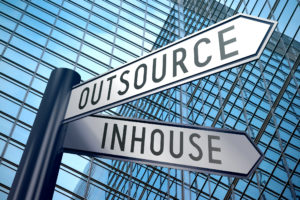 Against a background of tall office buildings, a signpost stands with two options: OUTSOURCE and INHOUSE.