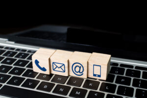 Small wooden blocks displaying symbols for a phone handset, envelope, at symbol and smartphone are lined up on a laptop keyboard, symbolizing multiple communication channels for Contact Center as a Service software.