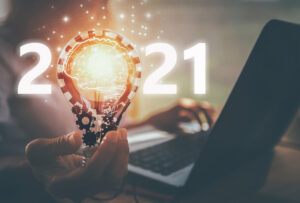 A person working at a laptop holding a lit lightbulb that serves as the zero in 2021. 