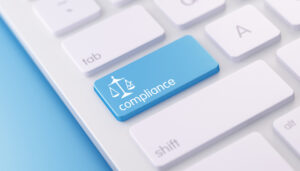 A close up of a white keyboard against a blue background with one light blue key that says "compliance" on it with a picture of a scale. 