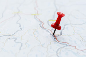 A close-up of a red thumbtack in a paper road map.