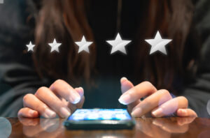 Close up of a person's hands as they use a smartphone lying on a table, with stars hovering to symbolize a review. 