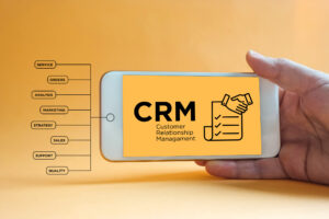 A close-up of a hand holding a smartphone that says CRM on the screen against a yellow background.