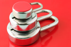 Three silver padlocks of decreasing size stacked largest to smallest against a red background, representing layered security.