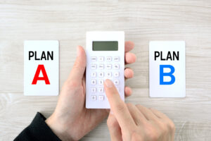 A person operates a calculator in between two pieces of paper. One paper says "Plan A" and the other says "Plan B."