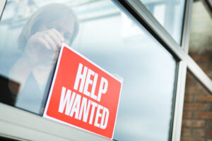 A woman places a red "Help Wanted" sign in a window.
