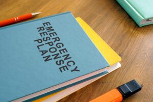 Close-up of a blue notebook on a wooden desk. The notebook's title says "Emergency Response Plan."