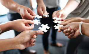 Closeup shot of a group of unrecognisable businesspeople holding puzzle pieces together.