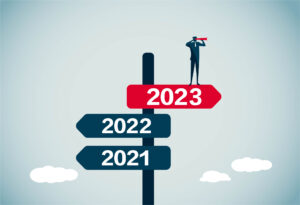 A tiny blue man in a suit stands on a street sign that says "2023" in red and points to the right/forward, while two other blue sections of the sign below him say 2022 and 2021 and point backward.