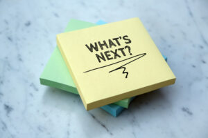 A pack of yellow post-it notes with "What's next?" written on the top note, stacked on top of green and blue post-its on a marble surface.