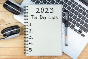 Overhead view of a spiral notepad resting on a laptop keyboard with "2023 To Do List" and a 5-point numbered list written on it.