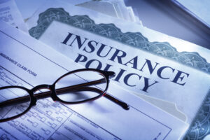 Close up of a paper that says "Insurance Policy" at the top with a pair of glasses resting on top of the paper.