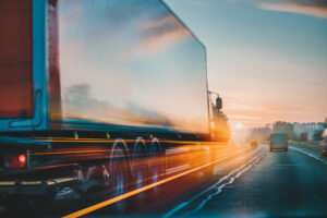 View of a semi truck driving toward the setting sun on a highway.
