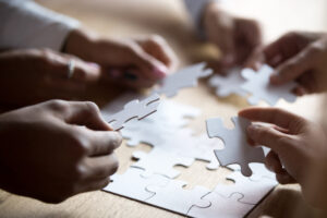 A close-up photo of multiple people's hands completing an all-white puzzle.