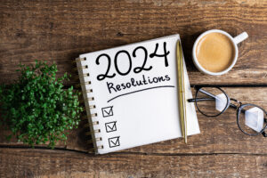 A pad of paper on a desk reads "2024 Resolutions" with three checkboxes under the heading.