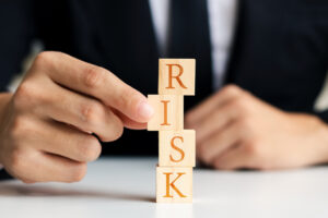 A person in a suit and tie stacks four wooden blocks that spell "RISK." 