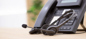 Close up of an office phone with a headset on a desk, representing contact center and call center work.