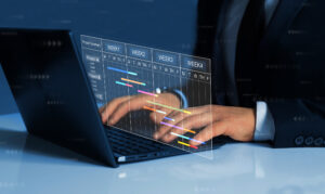 Close up of a person in a suit and tie working on a laptop with a project management timeline hovering over the keyboard.