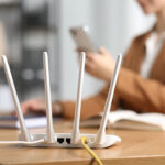 NSA Warns: Why Restarting Your Router Matters for Cybersecurity Executive Summary Woman with smartphone at table indoors, focus on Wi-Fi router